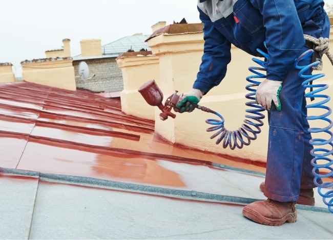 Worker spray-painting metal roof during maintenance